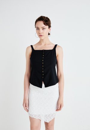 Zwart cropped tanktop met knoopdetails aan de voorkant, gecombineerd met een witte kanten minirok met een scalloped zoom.