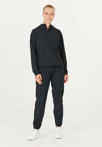 Completo sportivo nero composto da una giacca con zip e cappuccio, dotata di tasca a marsupio, e pantaloni jogger a vestibilità comoda con polsini e vita elasticizzati.