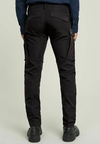 Black cargo pants made of durable fabric, featuring side pockets, a slim fit design, and a smooth texture. Worn with black boots.