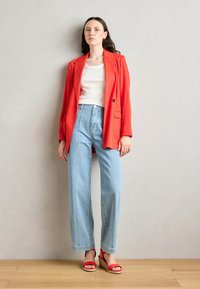Blazer rosso su misura sopra una camicia bianca, abbinato a jeans chiari a vita alta e sandali con zeppa rossi. Tessuto morbido e taglio dritto.