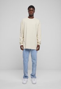 Tricou crem cu mâneci lungi, asortat cu blugi drepți albaștri deschiși și teniși albi. Design simplu, cu o croială lejeră și o textură moale.