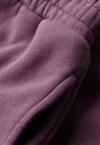 Nærbillede af lilla stof, der viser en rynket elastisk taljebånd og en sidesømslomme på blødt tekstureret tøj.