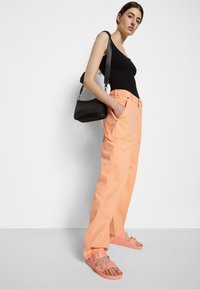 Calças largas de cor laranja claro com bolsos frontais, combinadas com sandálias rosas e uma mala de ombro preta. O top é uma camisola preta justa.
