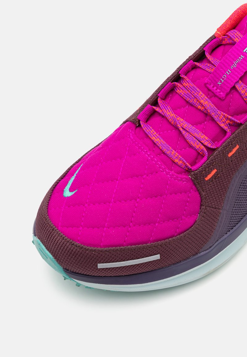 Sportschuh mit einem rosa gesteppten Obermaterial, braunen Akzenten, bunten Schnürsenkeln, gepolstertem Kragen und einer strukturierten Sohle mit türkisfarbenen Details.