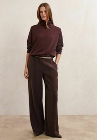 Pulover cu guler înalt, vinete, cu mâneci lungi, asortat cu pantaloni largi cu talie înaltă. Textură fină, design minimalist și croială lejeră.