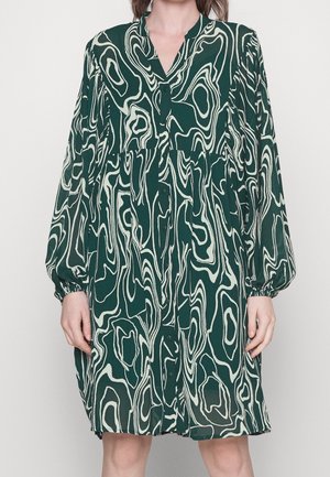 Robe verte à manches longues avec motif tourbillonnant blanc abstrait, boutonnée sur le devant et taille froncée, portée par une personne debout.
