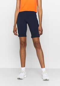 Marineblauwe fietsbroek gemaakt van rekbaar materiaal. Heeft een aansluitend ontwerp en een klein logo op de linker dij. Draag het met een oranje top.