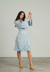 Hellblaues Kleid mit aufwendigen Spitzenmustern und ausgestellten Ärmeln. Das Design verfügt über eine taillierte Passform und einen knielangen Saum.