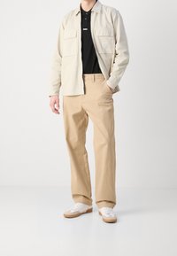 Beżowe spodnie w połączeniu z czarnym polo i jasnobeżową kurtką. Kurtka ma dwie przednie kieszenie i luźny krój. Całość dopełniają białe trampki.