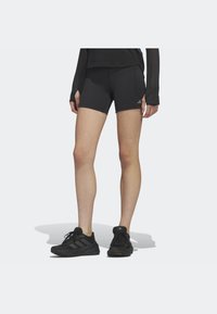 Pantalones cortos deportivos negros con un diseño ajustado y detalles de costura, combinados con zapatillas deportivas negras que cuentan con una suela texturizada y un logo.