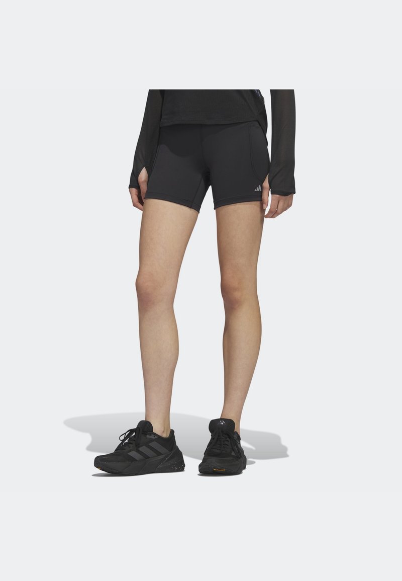 Pantalones cortos deportivos negros con un diseño ajustado y detalles de costura, combinados con zapatillas deportivas negras que cuentan con una suela texturizada y un logo.