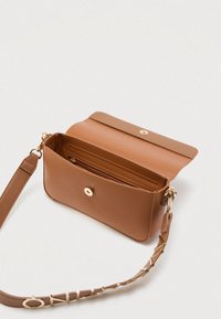Brązowa skórzana torba na ramię z magnetyczną klapką, wewnętrzną kieszenią na zamek, przeszywanymi miejscami na karty oraz paskiem z złotymi literami jako ozdobą.