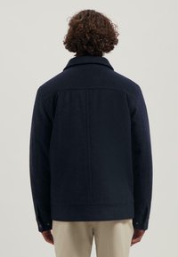 Marineblauwe wollen jas met een zachte, gestructureerde oppervlakte, voorzien van een klassieke kraag, rugnaad en knoopmanchetten. Eenvoudig, functioneel ontwerp.