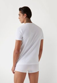 T-shirt bianca in cotone con maniche corte, texture liscia e collo a giro, abbinata a boxer bianchi. Modello visto da dietro.