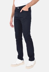 Chino blu navy con taglio slim, dotati di tasche frontali, chiusura con bottone e una texture liscia. Abbinati a sneaker bianche.
