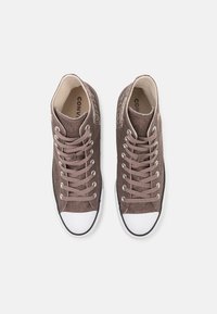 Bruna kanvas hög-top sneakers med vita gummitåhattar, svarta accenter och matchande snören, med en texturerad yta och tygfoder.