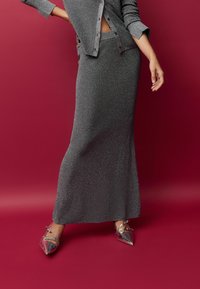 Pilkas, blizgantis, prigludęs sijonas ir atitinkama marškinėlių palaidinė. Apranga pasižymi elegantišku dizainu, lygia tekstūra ir blizgiomis detalėmis.