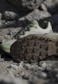 Chaussure de randonnée vert clair et beige avec une semelle Continental marron robuste reposant sur un terrain rocheux.