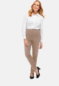 Lichtbeige op maat gemaakte broek met een gladde textuur, zijzakken en een subtiele gouden gesp, gecombineerd met een witte overhemd met lange mouwen en knopen.