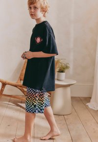 Svart bomulls t-shirt med en grafisk logotyp på bröstet, kombinerad med flerfärgade rutiga shorts med ett gradientmönster.