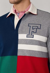 Farbblockiertes Poloshirt mit Abschnitten in Marineblau, Grau, Grün und Rot; weiße Streifen, Kragen mit rot-weißer Streifenmuster und gesticktem Buchstaben F.