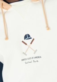 Sudadera blanca con mangas azul marino, que presenta un diseño bordado de un casco de seguridad y herramientas cruzadas. El texto incluye "Estados Unidos de América" y "Parque Nacional."