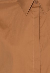 Brązowa koszula na guziki wykonana z gładkiej tkaniny, z wyraźnym kołnierzykiem, przednią listwą z jednym guzikiem oraz widocznym przeszyciem.