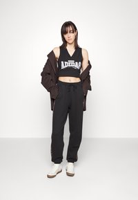 Fekete rövidített tank top, amelyen az "ADIDAS" logó látható, fekete jogger nadrággal, amelynek húzózsinóros dereka és oldalsó mintázata van, fehér sneakers-szel kiegészítve.