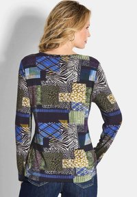 Langärmliges Oberteil mit einem multifunktionalen Stoff, der Tierdrucke und geometrische Designs in Grün, Blau, Schwarz und Beige zeigt.