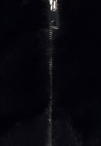 Gros plan sur un tissu noir flou avec une fermeture éclair en argent brillante partiellement visible qui court verticalement au centre.