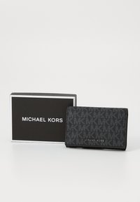 Portefeuille noir à motif fabriqué en matériau texturé, avec un design à rabat, une marque "MICHAEL KORS" en argent, et une boîte cadeau noire.