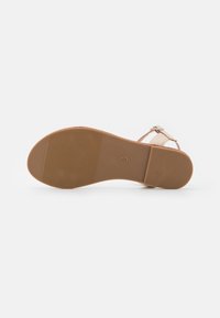 Vaalean beige sandaalit, joissa on teksturoitu ruskea kumipohja. Ominaisuudet ohuista remmeistä ja säädettävästä soljesta varmistaakseen mukavan istuvuuden.