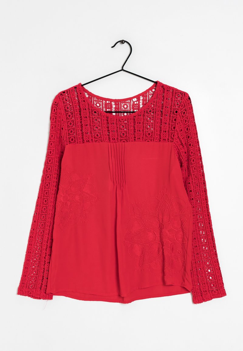 Blouse rouge à manches longues avec des détails en dentelle sur les manches, broderies florales sur le devant, plis au niveau du col et un ourlet arrondi.