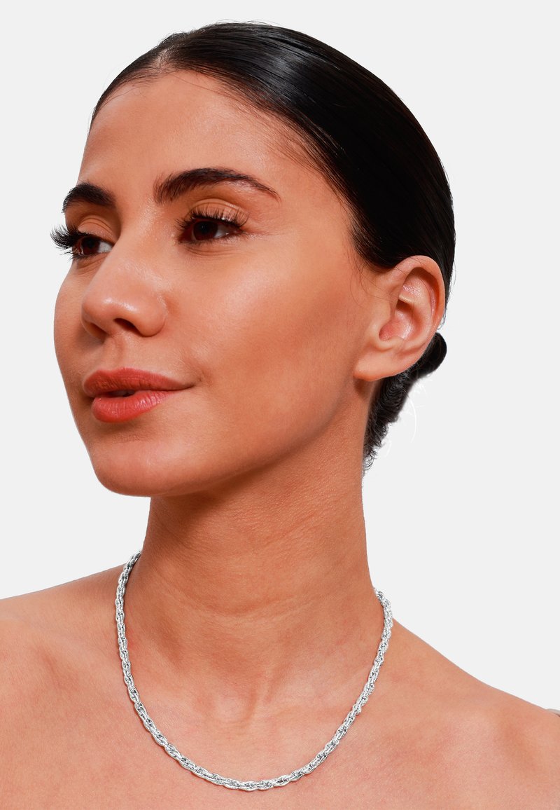 Collana a catena twist in argento esposta su pelle nuda, caratterizzata da una texture liscia e un design intrecciato, che riflette la luce in modo efficace.