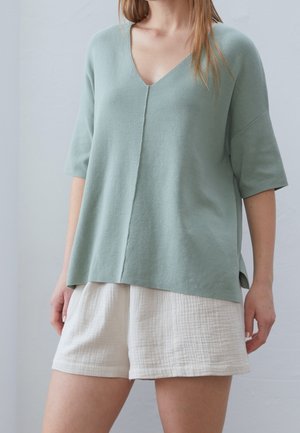 Haut vert clair à manches courtes et décolleté en V, avec une coupe droite et une coupe décontractée, assorti à un short blanc texturé. Tissu doux et respirant.