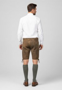 Pantaloni corti in pelle marrone con lacci laterali, abbinati a calze verdi fino al ginocchio e scarpe marroni, completati da una camicia bianca con bottoni.