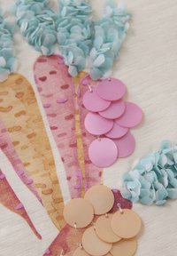 Textiel met een kleurrijk abstract ontwerp met roze, oranje en paarse strepen. Inclusief blauwe stofaccenten en ronde labels in roze en beige.