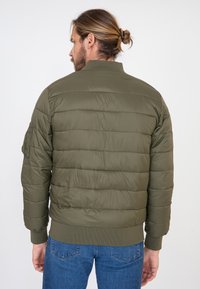 Oliwkowa, pikowana kurtka z poziomym przeszyciem, prążkowanymi mankietami i kołnierzem. Posiada boczną kieszeń na lewym rękawie.