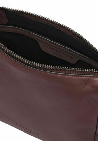 Burgundowy portfel na zamek błyskawiczny ze skóry o gładkiej fakturze, czarne wnętrze i zamek w odcieniu srebra. Logo wytłoczone wewnątrz. Brak widocznych wzorów.