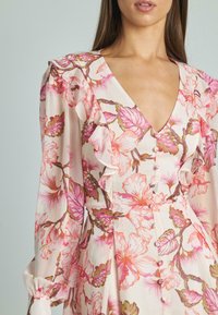 Vestido floral de tela rosa claro con mangas con volantes, escote en V profundo y cierre de botones. Presenta grandes patrones florales en rosa y verde.