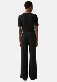 Zwart aansluitend shirt met korte mouwen en een naad aan de achterkant, gecombineerd met losse, hooggesneden zwarte broek met een gladde textuur.