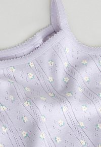 Jasnofioletowy dzianinowy top na cienkich ramiączkach z falistymi brzegami i małym białym oraz zielonym wzorem kwiatowym.