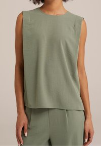 Bez rękawów, teksturowany top w kolorze szałwii oraz pasujące spodnie, noszone przez osobę o jasnobrązowej skórze na neutralnym tle.