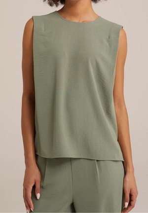 Top senza maniche di un verde salvia testurizzato e pantaloni abbinati indossati da una persona con pelle di colore marrone chiaro su uno sfondo neutro.