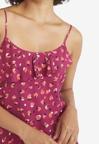 Lila ärmelloses Top mit Rüschendetail an der Vorderseite, das ein Blumenmuster in den Farben Orange, Pink und Schwarz aufweist. Weicher Stoff.