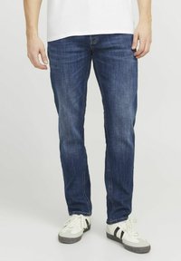 Dunkelblaue Jeans aus Denim im Slim-Fit, mit normalen Taschen, dezenten Nähten und abgenutzter Textur. Kombiniert mit weißen und schwarzen Sneakers.