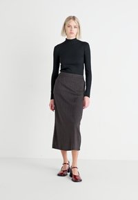 Črna rebrasta turtleneck je kombinirana s temno sivo midi krilo s tankimi črtami. Manekenka nosi vino rdeče čevlje z nizko peto in zankami okoli gležnjev.