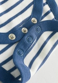 Body en tissu rayé blanc et marine, avec col rond, boutons-pression métalliques et bordure bleue. Texture douce en coton.