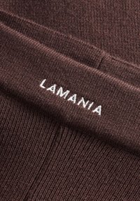 Tamsiai rudos spalvos gumbuota medžiaga su balta siuvinėta "LAMANIA" logo. Audinys yra minkštas ir šiek tiek tamprus, turi juostuotą dizainą.