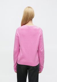 Pulover roz confecționat din material tricotat moale, cu decolteu rotund și manșete striate. Spatele are un finisaj neted, neornamentat.